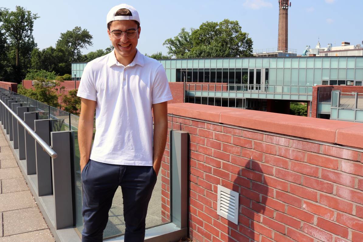 Alberto laughs while standing on rooftop with brick backdrop