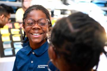 A young boy in a navy blue shirt smiles while wearing eyeglasses