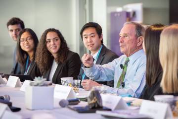 Former New York City Mayor Michael Bloomberg and Johns Hopkins students sit together at a long conference room table