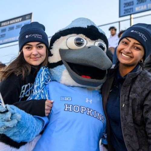 Two students pose with Jay, the Johns Hopkins Blue Jay mascot, in the stands at Homewood Field
