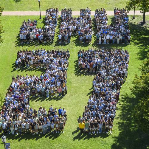 Hundreds of students are arranged to spell JHU27 on a green campus quad