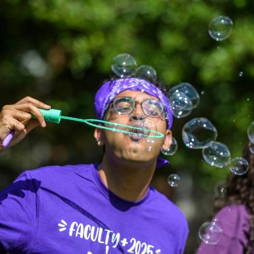 A man in a purple shirt and bandana blows bubbles