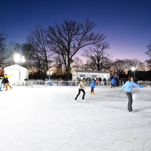 Skaters enjoy the JHU Ice Rink against the backdrop of a beautiful blue, purple, and orange sunset