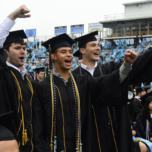 Three students in cap and gown cheer