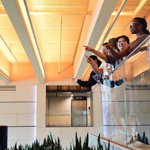 A group of people smile and point while looking over a balcony in the interior of a modern building