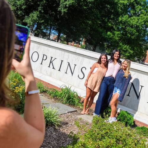 Three people pose in front of a Johns Hopkins University sign